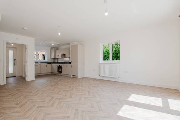A spacious, empty room with a herringbone parquet floor and a window letting in natural light.