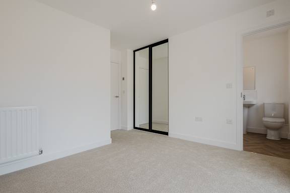 A white room with a carpeted floor and a white radiator on the wall.