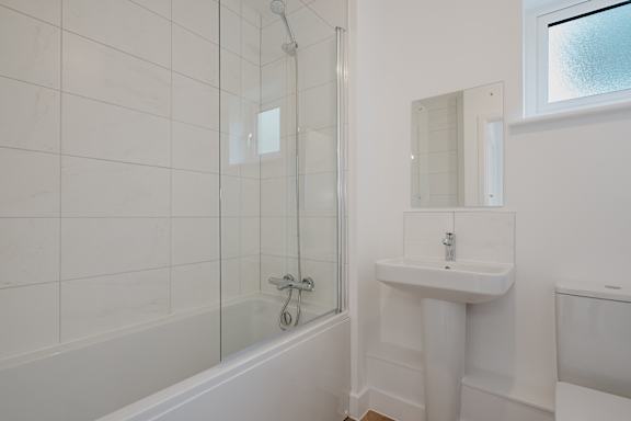 A white bathroom with a sink, mirror, and bathtub.
