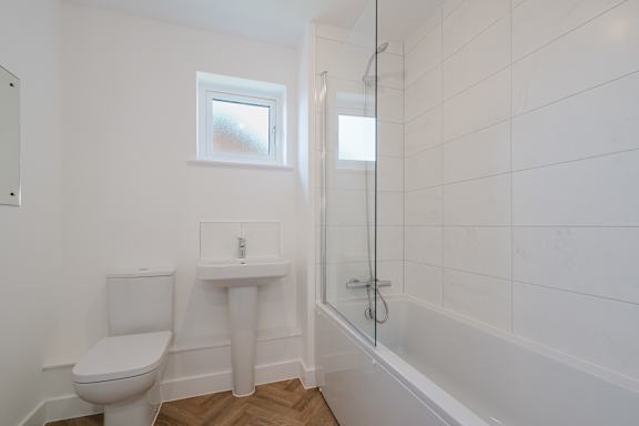 A white bathroom with a toilet, sink, and shower.