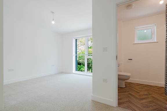 A white room with a window and a toilet in the hallway.