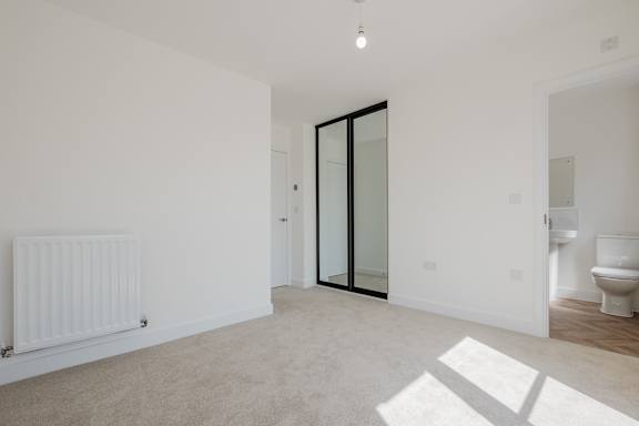 A white room with a carpeted floor and a white radiator on the wall.