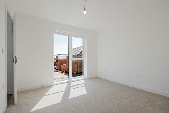 A room with a door leading to a balcony with a view of a building.