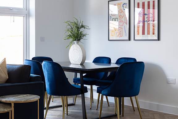A dining room with blue chairs and a white vase with a plant in it.