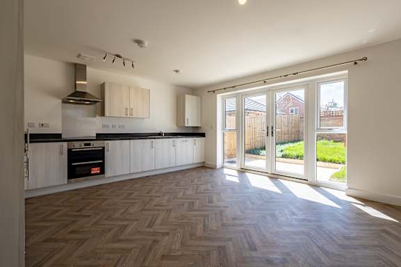 A kitchen with a wooden floor and a view of a backyard through the sliding glass doors.