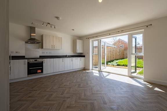 A kitchen with a wooden floor and a view of a backyard through the open door.