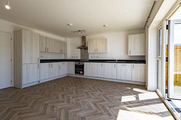 A modern kitchen with wooden flooring and white cabinets.