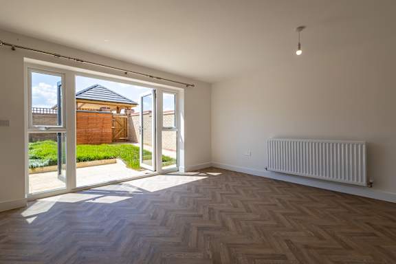 A room with a wooden floor and a white wall with a window and a door.