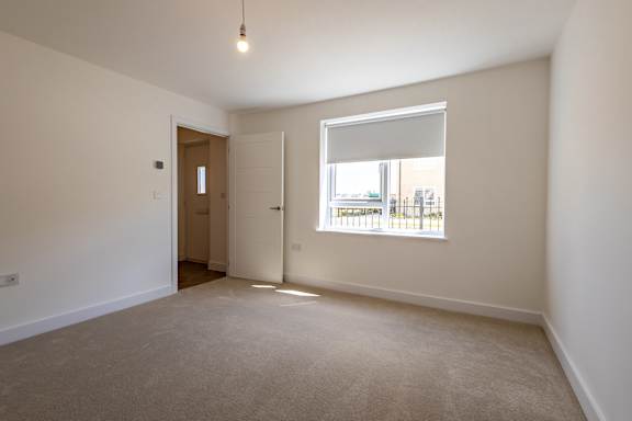 A room with a carpeted floor, a window with blinds, and a door leading to another room.
