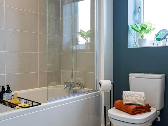 A white bathtub with a glass shower door and a toilet with a towel on top.