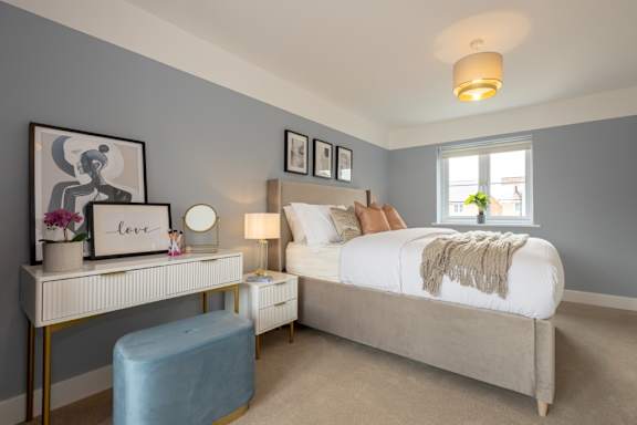 A bedroom with a bed, nightstand, and a desk with a lamp and a vase of flowers.