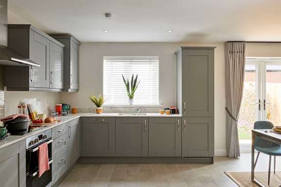 A kitchen with grey cabinets and a window with a plant on the windowsill.
