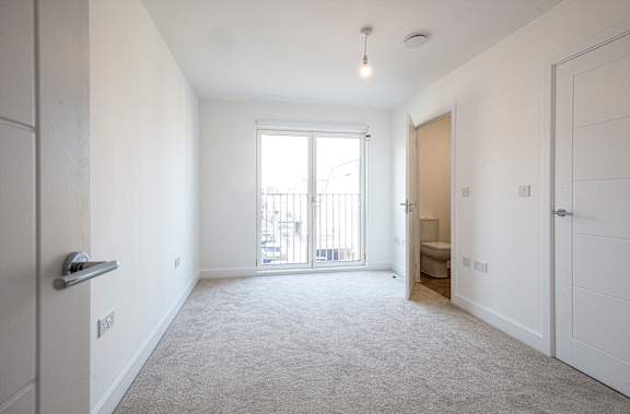 A spacious, empty room with a carpeted floor and a sliding glass door leading to a balcony.