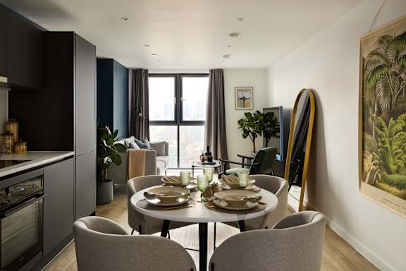 A modern dining room with a table set for two and a painting on the wall.