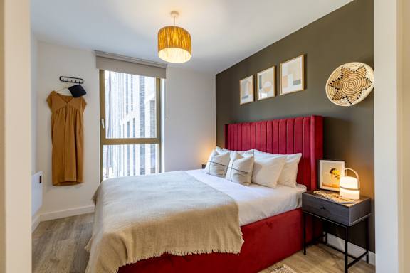 A bedroom with a red headboard and a bed with a white comforter.