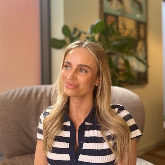A woman with long blonde hair is sitting on a couch wearing a striped shirt.