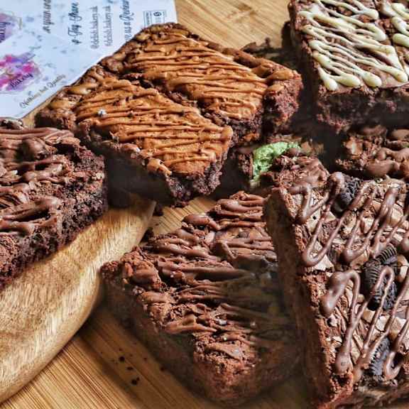 A wooden board with a variety of chocolate brownies on it.