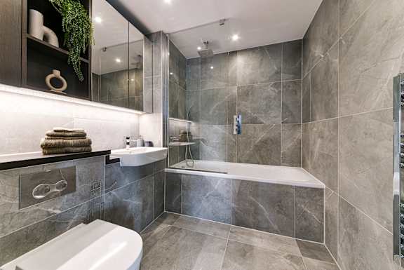 a bathroom with grey tiles and a tub and a sink