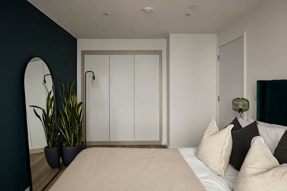 A bedroom with a bed, a mirror, and a potted plant.