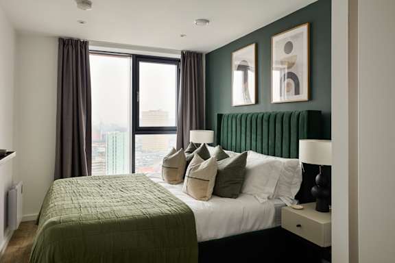 A bedroom with a large bed and a window overlooking a cityscape.