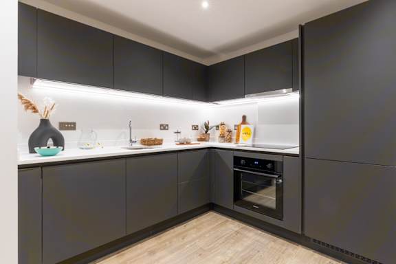 A modern kitchen with dark grey cabinets and a wooden floor.