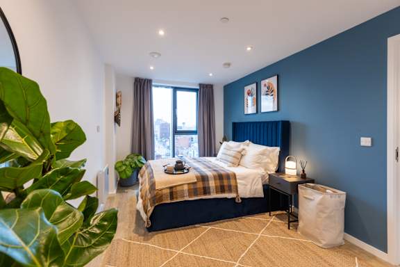 A bedroom with a bed, nightstand, and a plant.