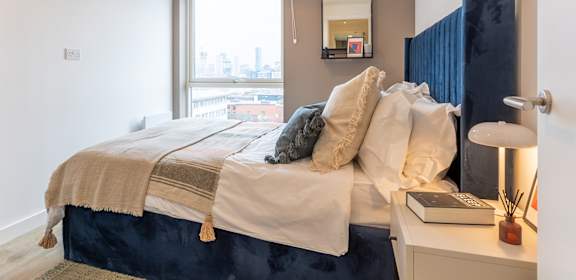 A bed with a white blanket and pillows is in front of a window.