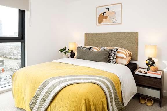 A bedroom with a bed covered in a yellow comforter and pillows.