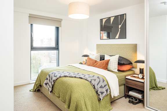 A bedroom with a bed, nightstand, and a large window.