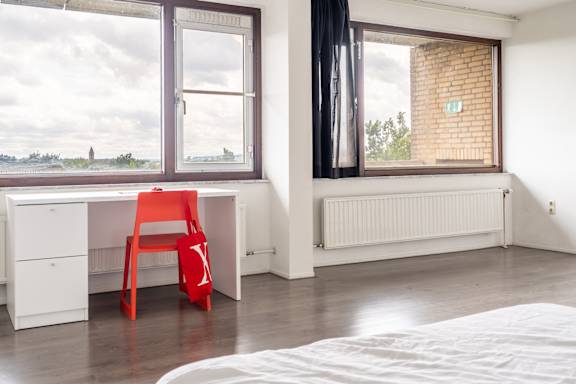 Floor Plan  A white desk with a red chair and a white radiator in a room with a window.