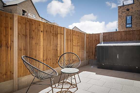 Two chairs are on a patio with a wooden fence.