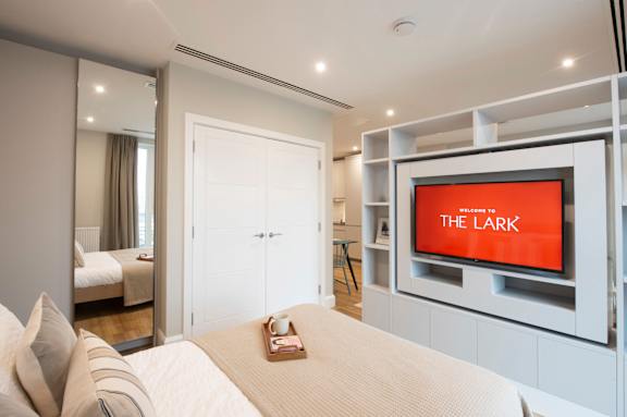 A bedroom with a bed, a dresser, and a television with the word "THE LARK" on it.