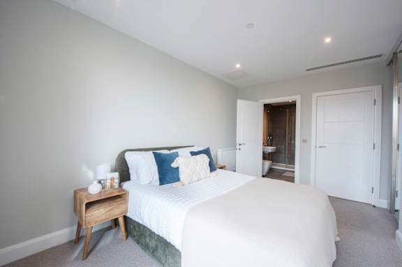A bedroom with a bed, nightstand, and a doorway leading to another room.