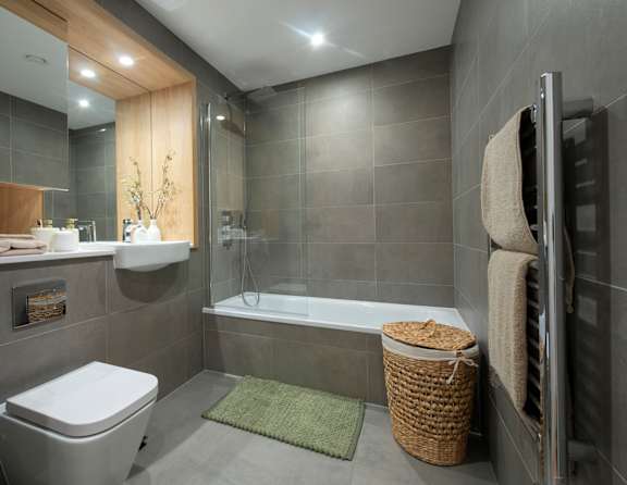 A modern bathroom with a white toilet, a bathtub, and a green rug.