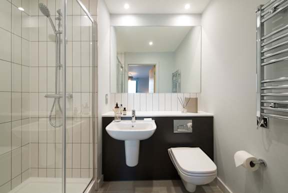 A modern bathroom with a walk-in shower, sink, toilet, and mirror.