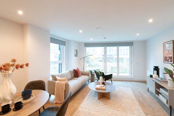 A living room with a white sofa, a wooden coffee table, and a large window.