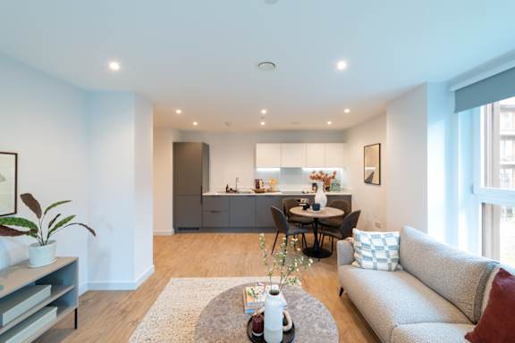 A modern living room with a grey couch, a coffee table, and a dining table set up.