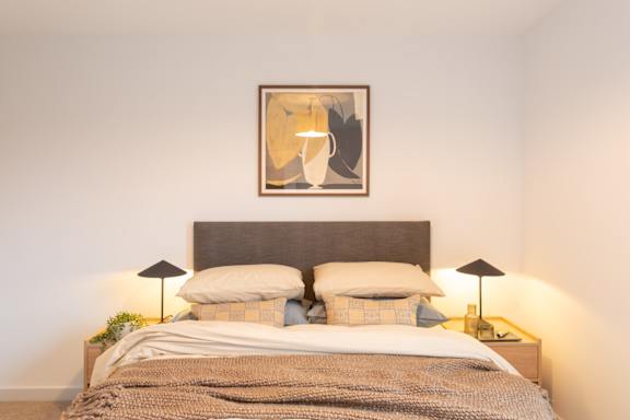 A bed with a grey headboard and a blanket with a pillow on it.
