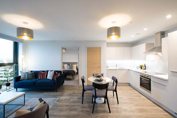 A modern living room with a blue couch and a dining table with four chairs.