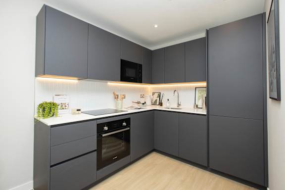 A modern kitchen with dark grey cabinets and a wooden floor.