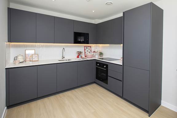 A modern kitchen with dark grey cabinets and a wooden floor.