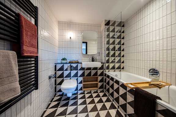 A black and white tiled bathroom with a towel rack on the left.