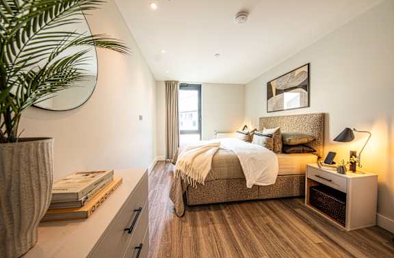 A bedroom with a large bed and a plant on the side table.
