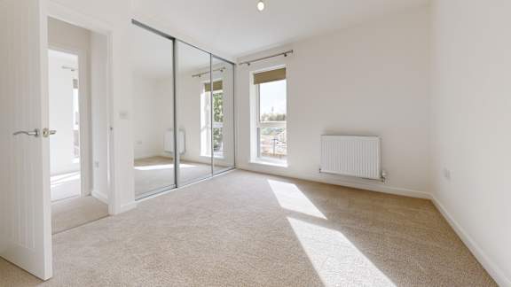 A room with a carpeted floor, a white wall, a sliding glass door, and a white radiator.