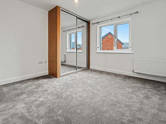 A room with a grey carpet and a large mirror on the wall.