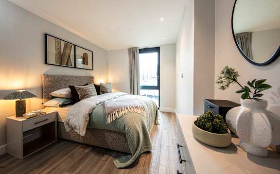 A bedroom with a bed, nightstand, and a plant.