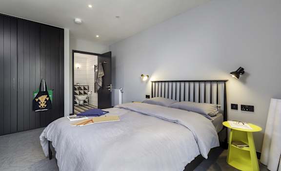 A bedroom with a bed, a yellow stool, and a black and white striped headboard at Beton Apartments, Wembley