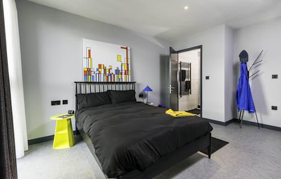 A bedroom with a bed, a yellow stool, and a blue umbrella at Beton Apartments, Wembley, HA9 0SL