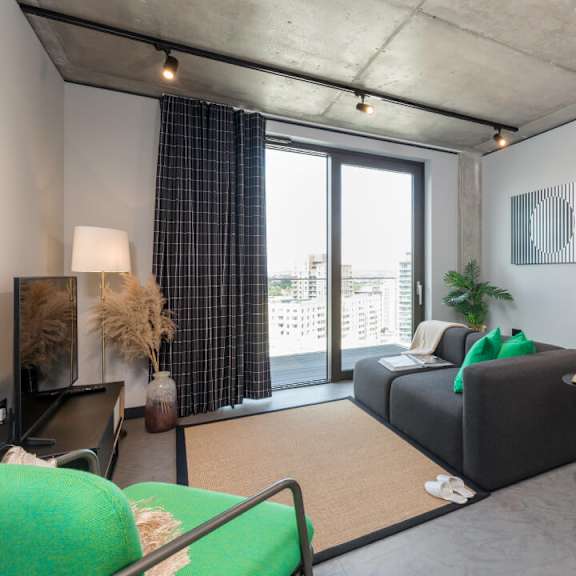 A living room with a grey couch and a green chair at Beton Apartments, Wembley, HA9 0SL