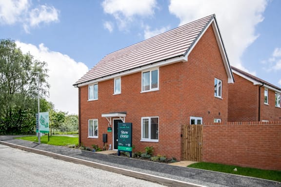 A red brick house with a green sign in front.